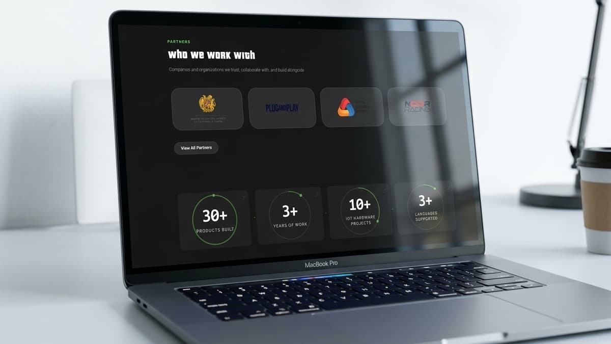 Laptop screen displaying a partners showcase page titled "who we work with" with four logo cards and four circular statistics dials showing products built and years of operation.Laptop screen displaying a partners showcase page titled "who we work with" with four logo cards and four circular statistics dials showing products built and years of operation.